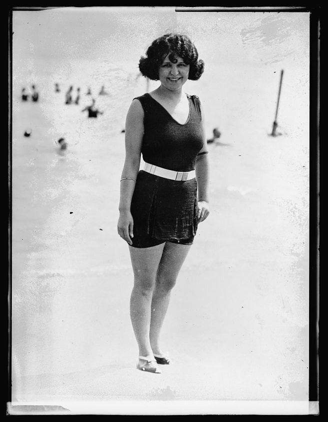 Black and white photograph of a woman wearing a bathing suit with no sleeves and a V-neck, ands shorts midway down her thighs. The tunic is long enough to almost cover the shorts.