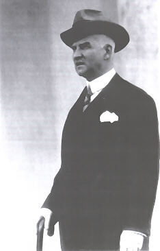 Black and white photograph of Emil Młynarski wearing a suit and hat and using a walking stick