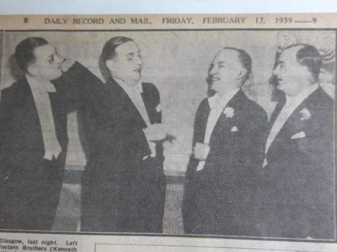 A newspaper clipping printed with the text 'Daily Record and Mail, Friday , February 17, 1939 ---- 9' and a photo of four men in white tie dinner suits chatting and laughing at a party. Two of the men are wearing monocles.