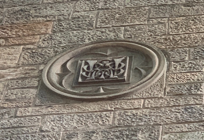 A carved stone plaque with with a large W embedded in a stone wall